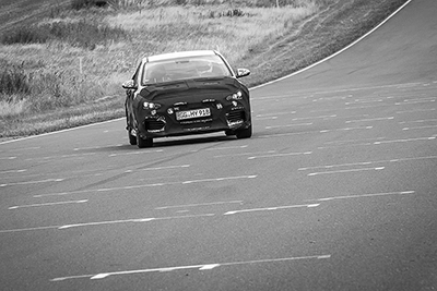 Schwarzer, getarnter Hyundai i30 Erlkönig fährt frontal auf einer Teststrecke oder Rennstrecke, detailliert sichtbar.